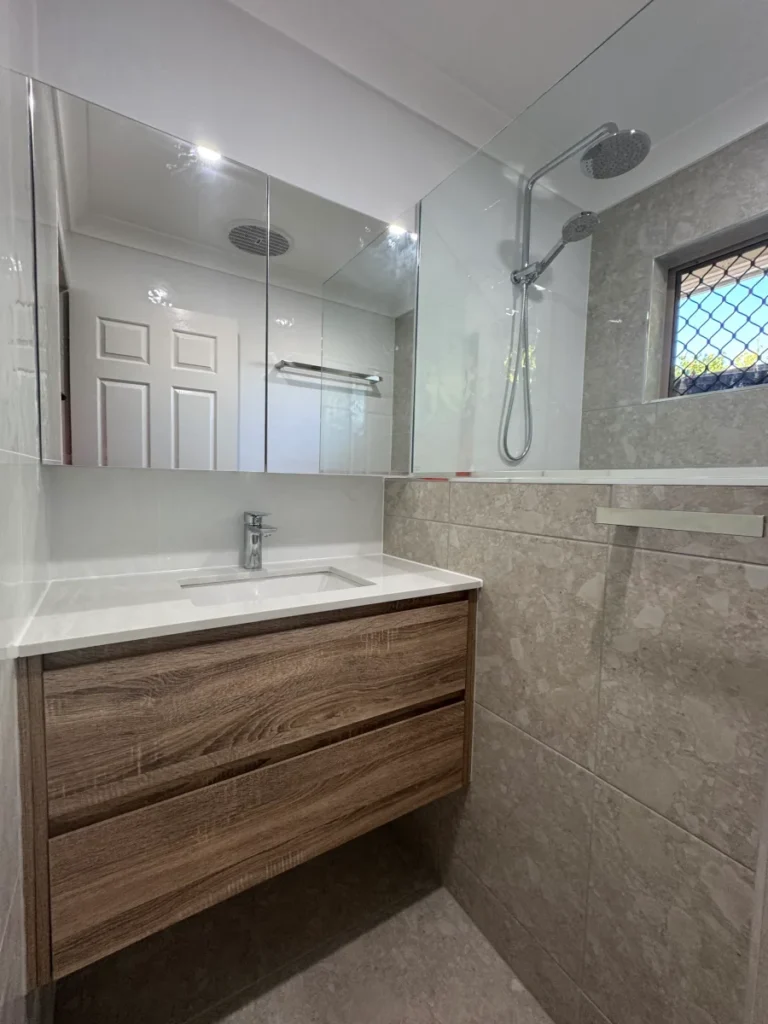 Grey and white tiled bathroom finished with a wall hung wooden cabinet, stone top and chrome fixtures