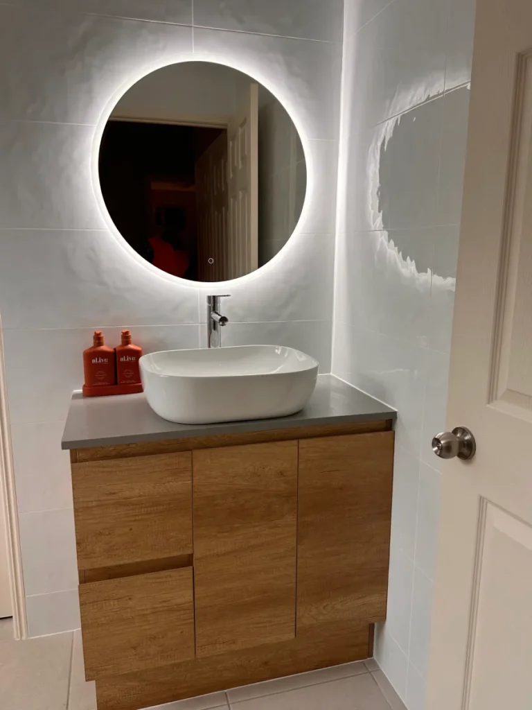 Round LED mirror, rippled white tiles and stone top vanity